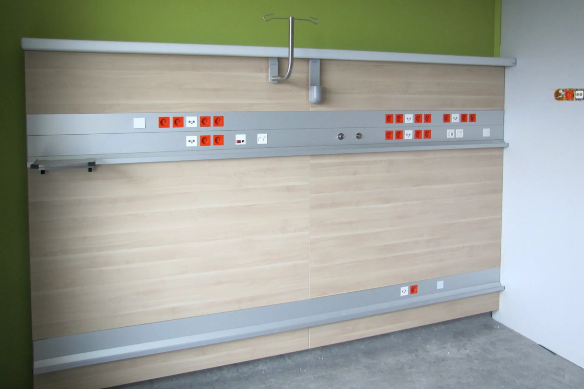 Wand mit mehreren Steckdosen und Anschlüssen in einem Raum mit grün gestrichener Wand und grauem Boden