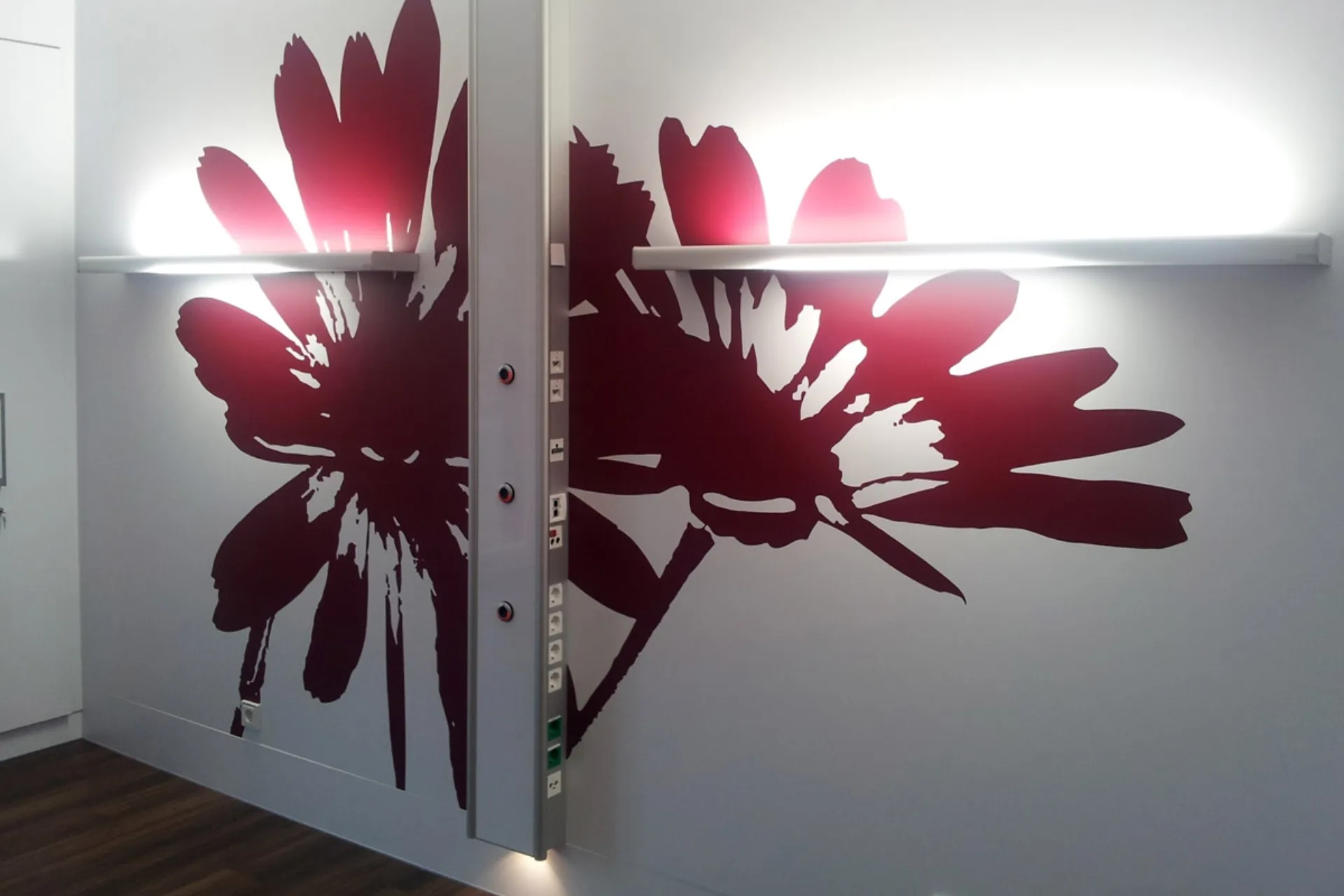 Großflächige dunkelrote Blütenmuster auf einer hellen Wand mit zwei horizontalen Leuchtleisten, die die Wand in der Mitte teilen