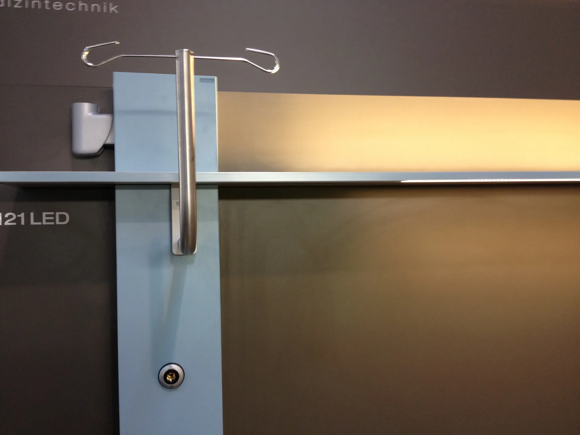 Detailaufnahme einer Versorgungseinheit pure mit hellblauer Front, vertikalem Chromgriff, Infusionshalter und medizinischem Gasanschluss vor dunklem Hintergrund