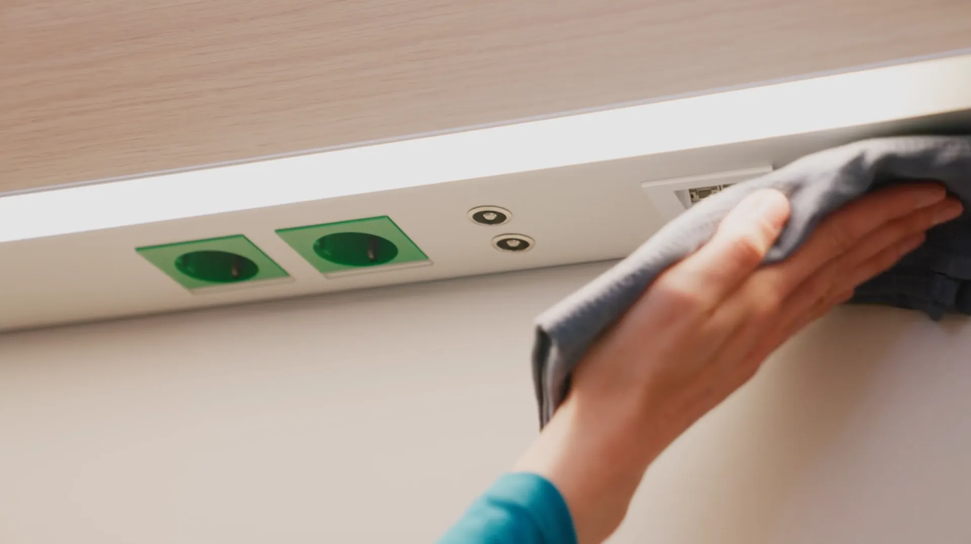 Nahaufnahme einer Hand mit Lappen, die über die flächenbündige Leiste mit Steckdose und Anschlüssen putzt